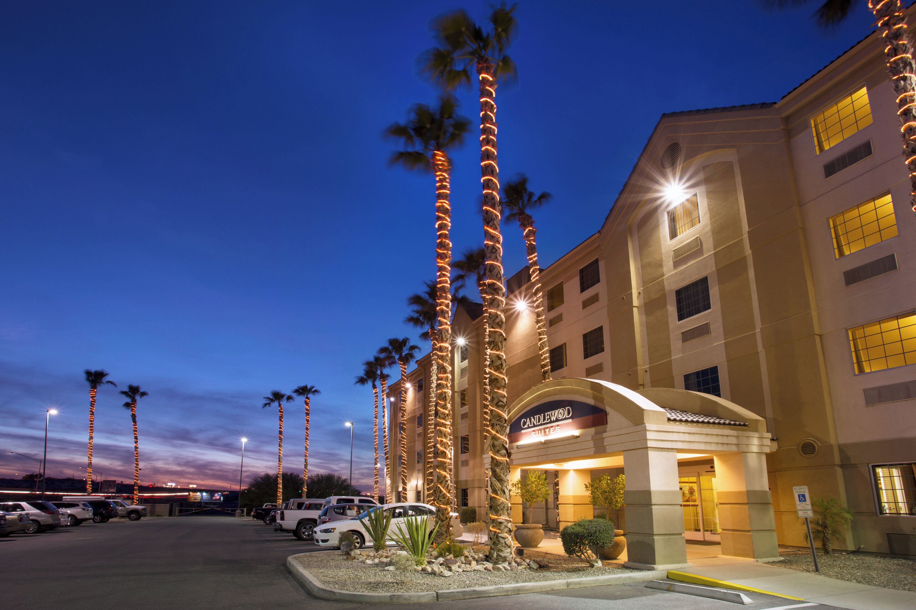 A hotel with a modern facade, palm trees, and a parking lot.