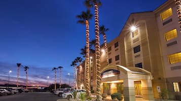A hotel with a modern facade, palm trees, and a parking lot.