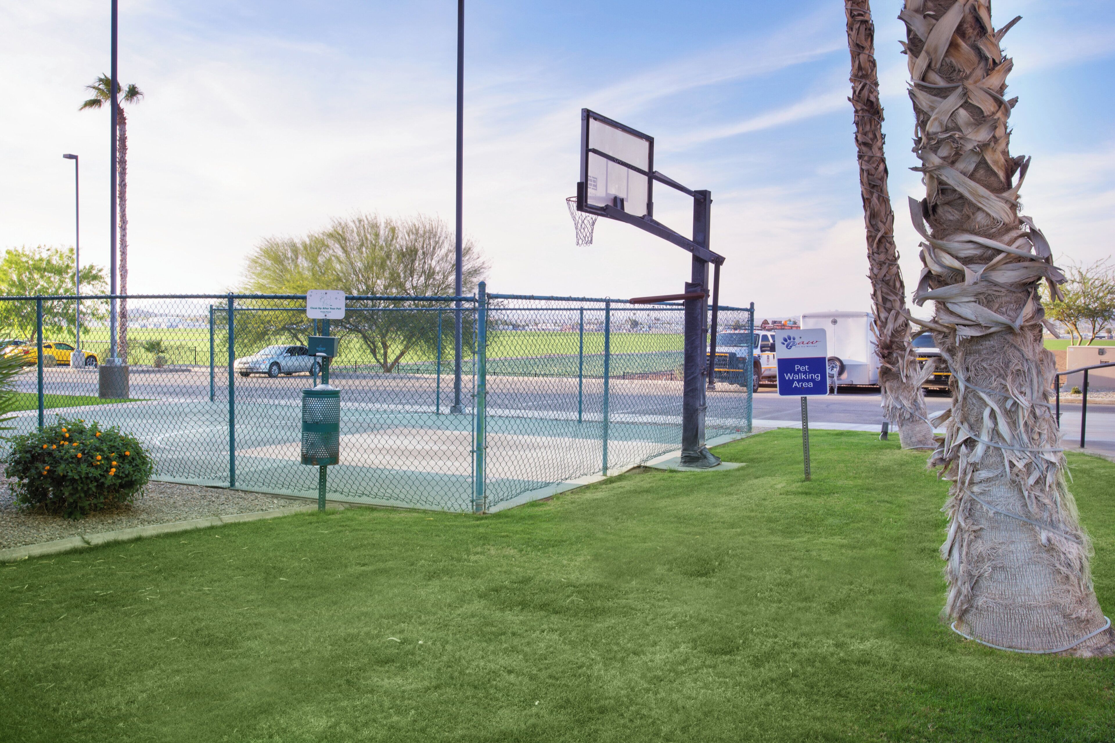 A fenced basketball court with a basketball hoop, a trash can, and a sign indicating a pet walking area.