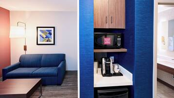 Habitación de hotel con sofá, una obra de arte abstracta enmarcada, microondas, cafetera y un cubo de basura.