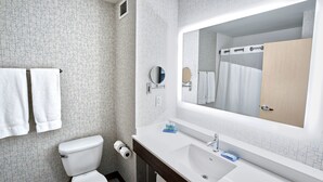 Un baño con inodoro blanco, lavamanos con espejo y dos toallas colgadas en un perchero.
