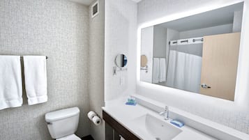 Un baño con inodoro blanco, lavamanos con espejo y dos toallas colgadas en un perchero.