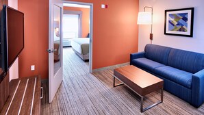 Habitación de hotel con un escritorio de madera, un sofá azul, una lámpara y una cama al fondo.