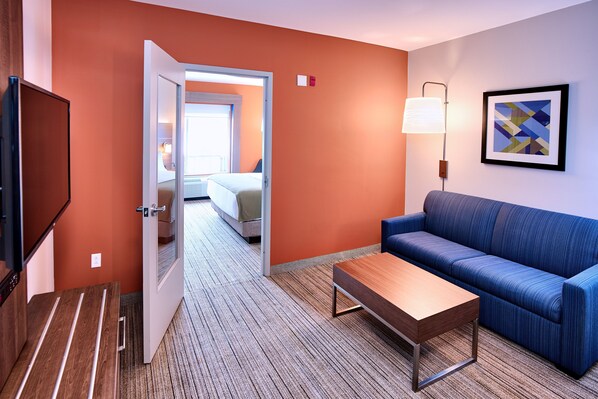 A hotel room with a wooden desk, a blue sofa, a lamp, and a bed in the background.