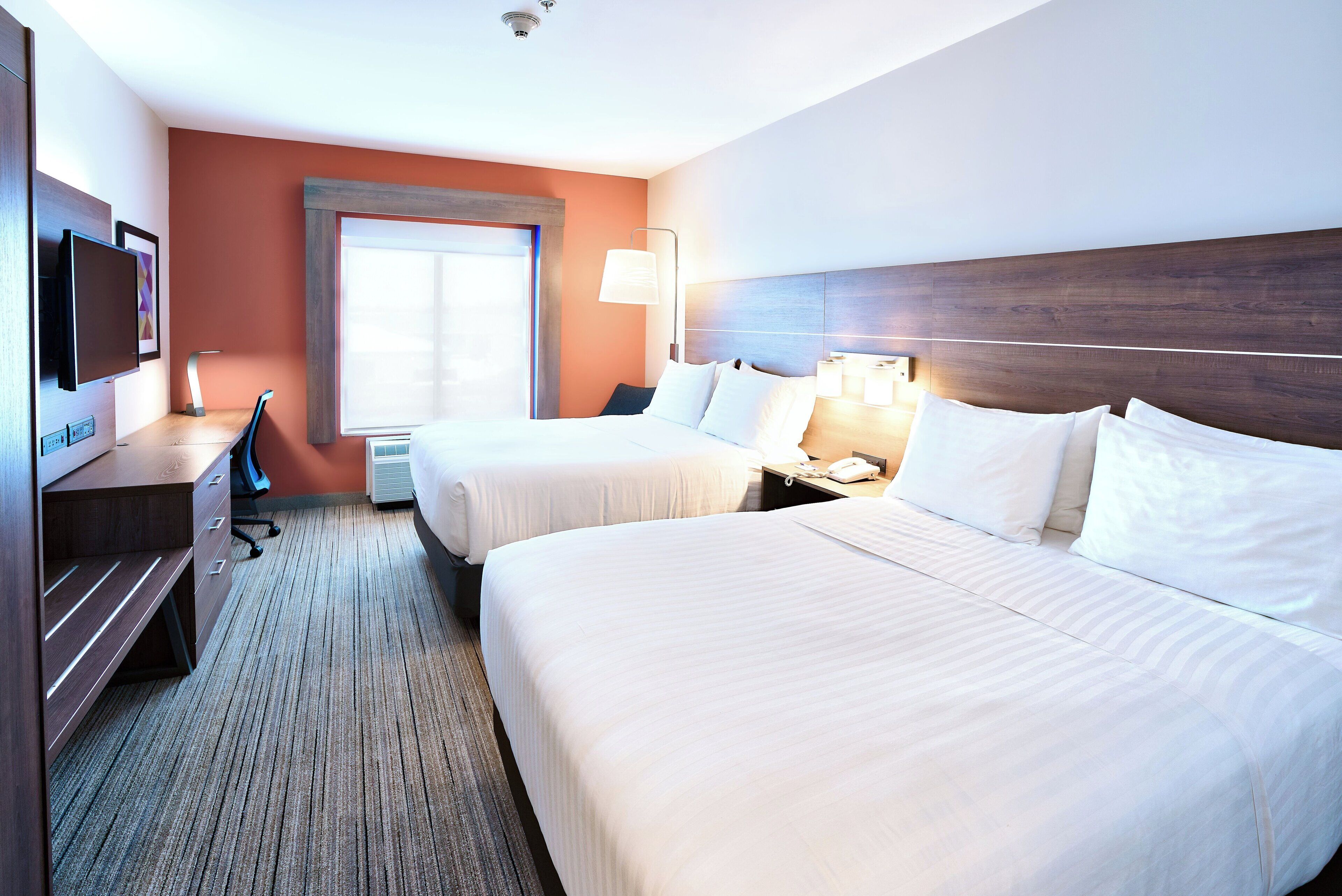 Een hotelkamer met twee bedden, een bureau met stoel, een televisietoestel en een raam met zonwering.