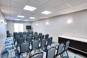 Une salle de conférence avec des rangées de chaises, un écran de projection et un tableau blanc.