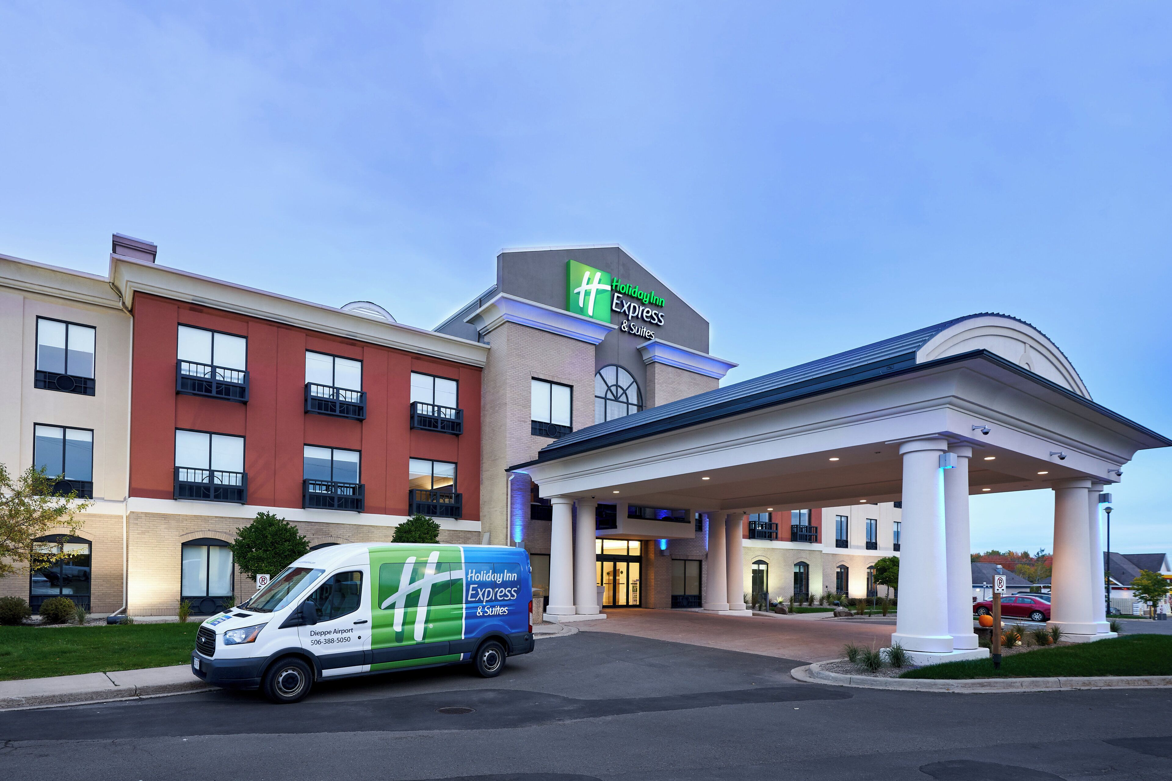 A Holiday Inn Express & Suites hotel with a modern design, a covered entrance, and a van parked in front.