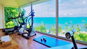 A gym with exercise equipment and a large window overlooking a beach. - The Sunset Beach Resort & Spa Taling Ngam (Koh Samui)