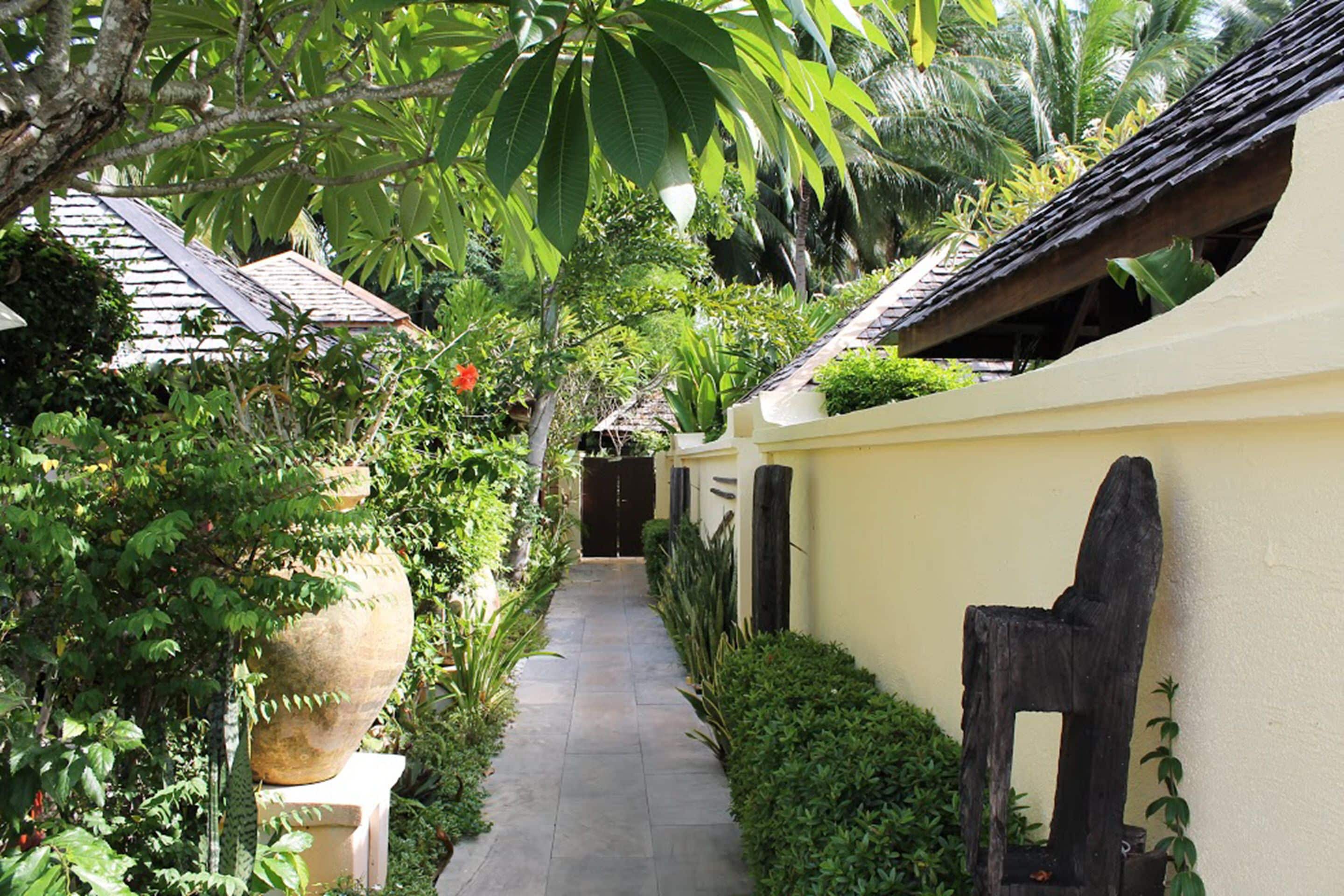 A narrow pathway flanked by lush greenery and traditional architecture.