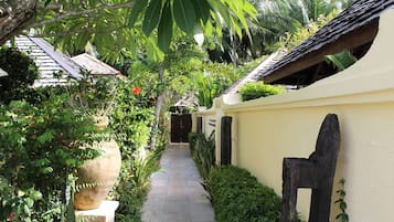 A narrow pathway flanked by lush greenery and traditional architecture.