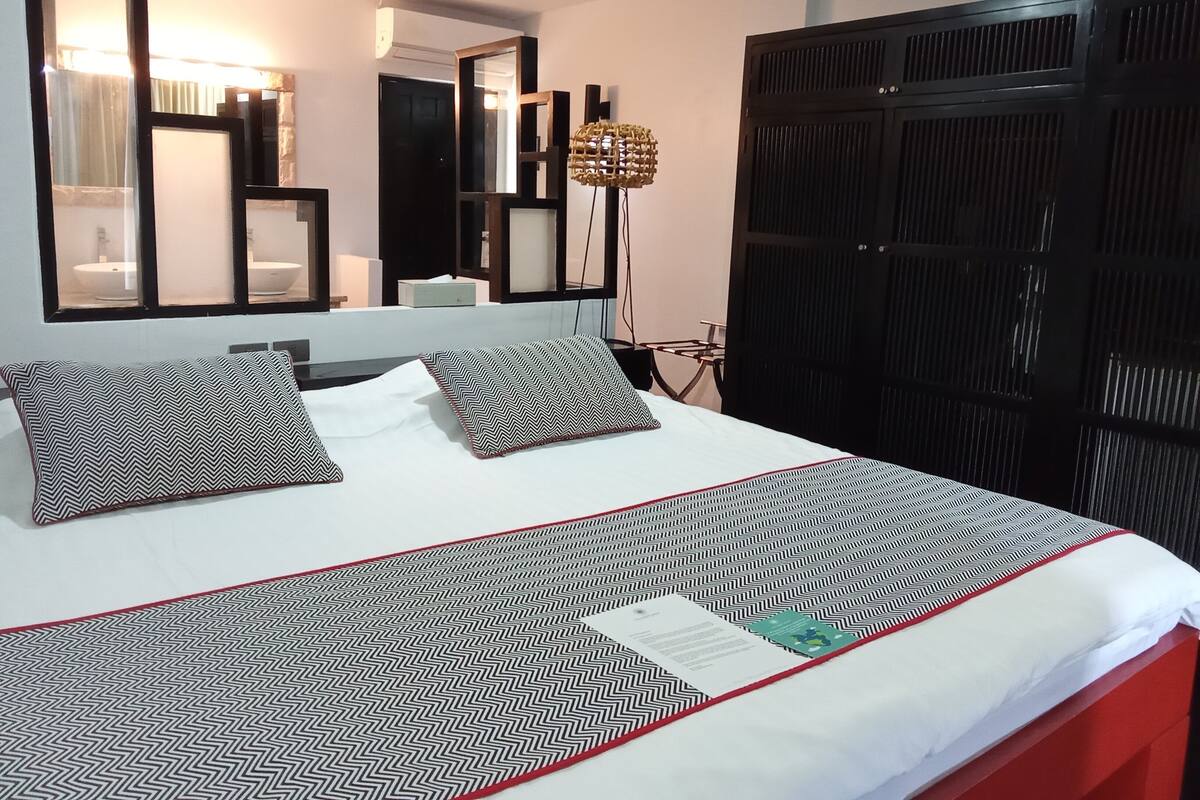 A neatly made bed with patterned pillows, a bedside table, and a large mirror above it.