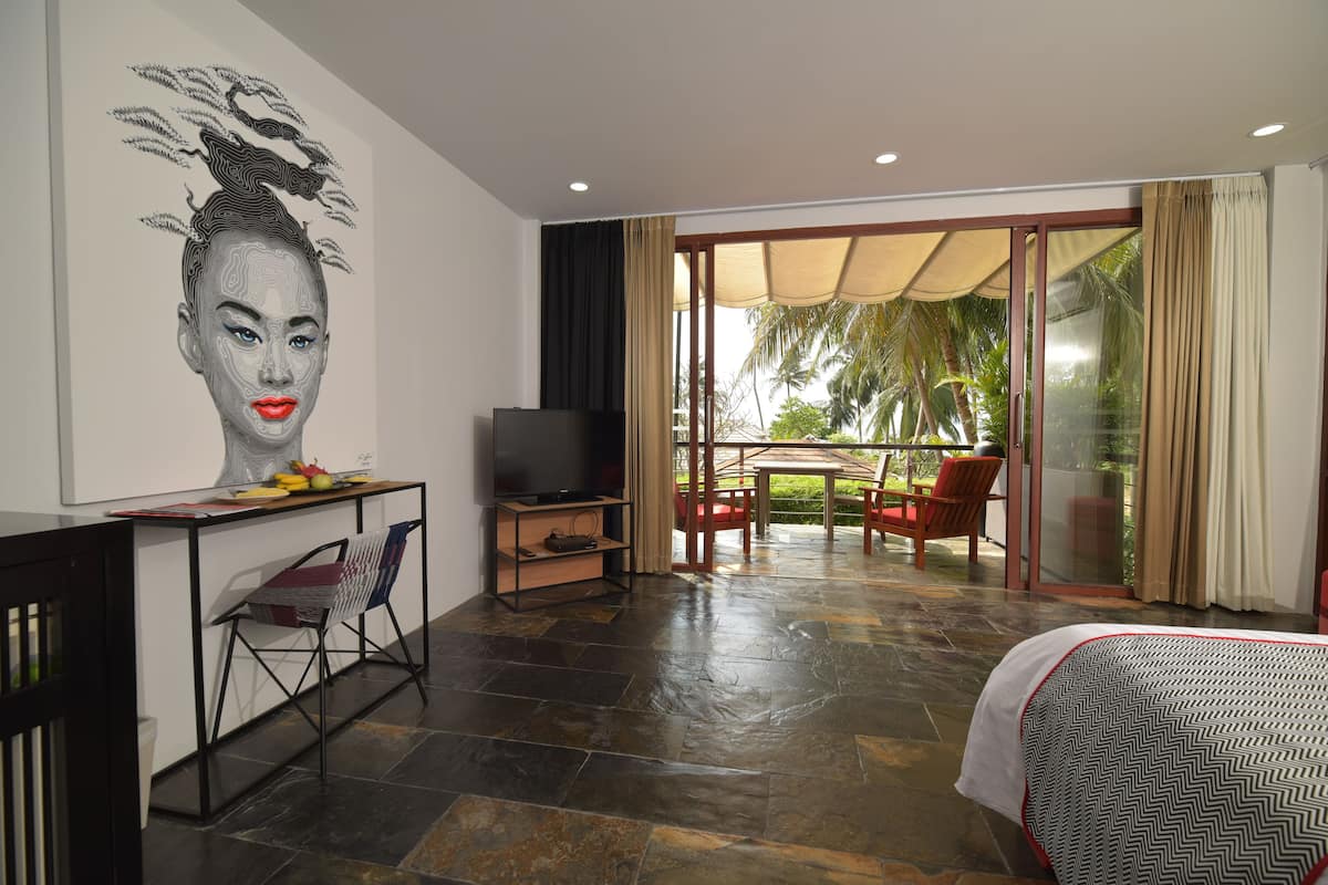 A hotel room with a bed, a desk with a television, a chair, and a view of the outdoors.