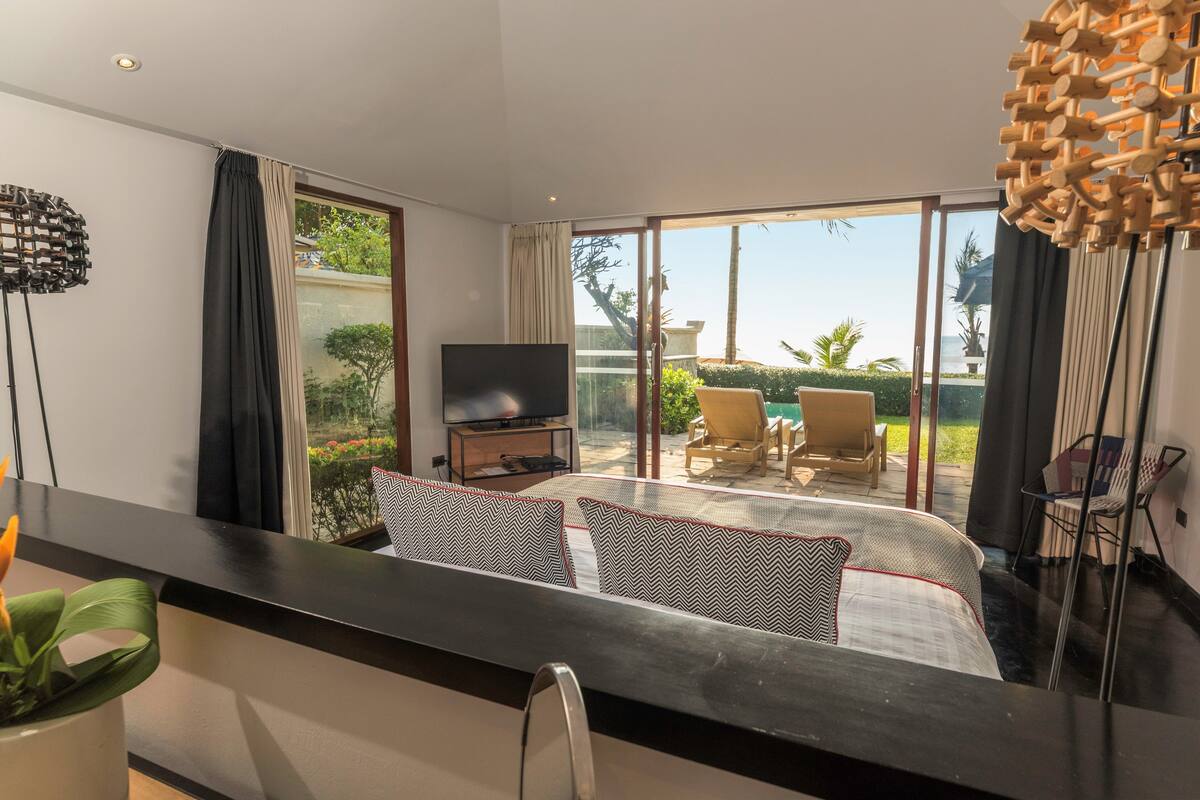 A modern hotel room with a large bed, a TV, and a balcony with outdoor seating.