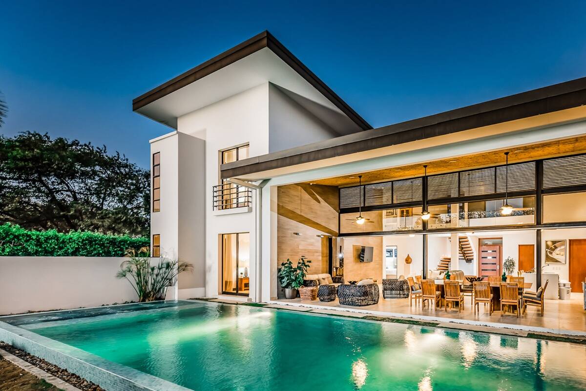 A modern house with a swimming pool, large windows, and a dining area.