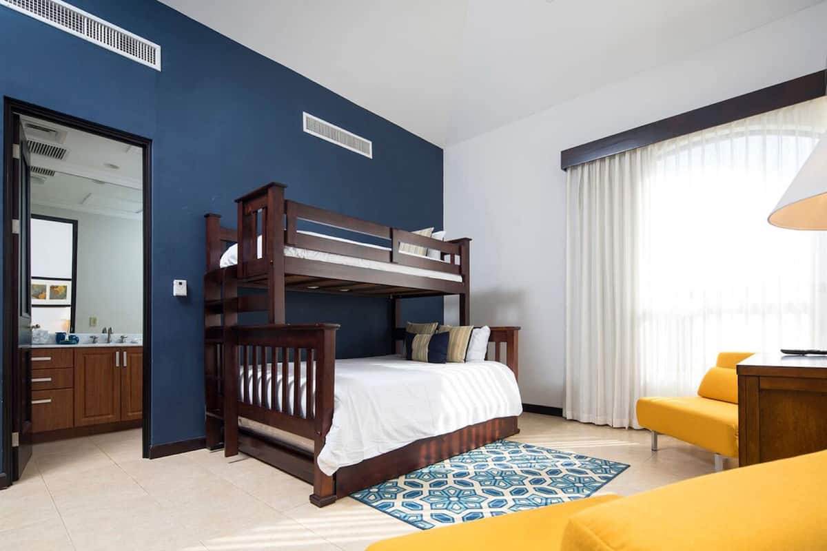 A room with a bunk bed, a desk, a chair, a patterned rug, and a large window with curtains.