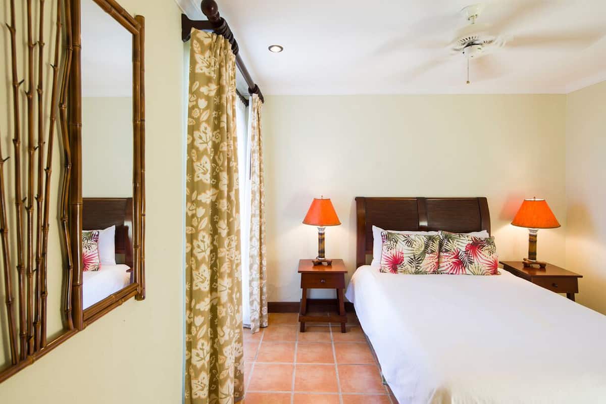 A hotel room with a bed, two bedside tables with lamps, a large mirror, and a window with curtains.