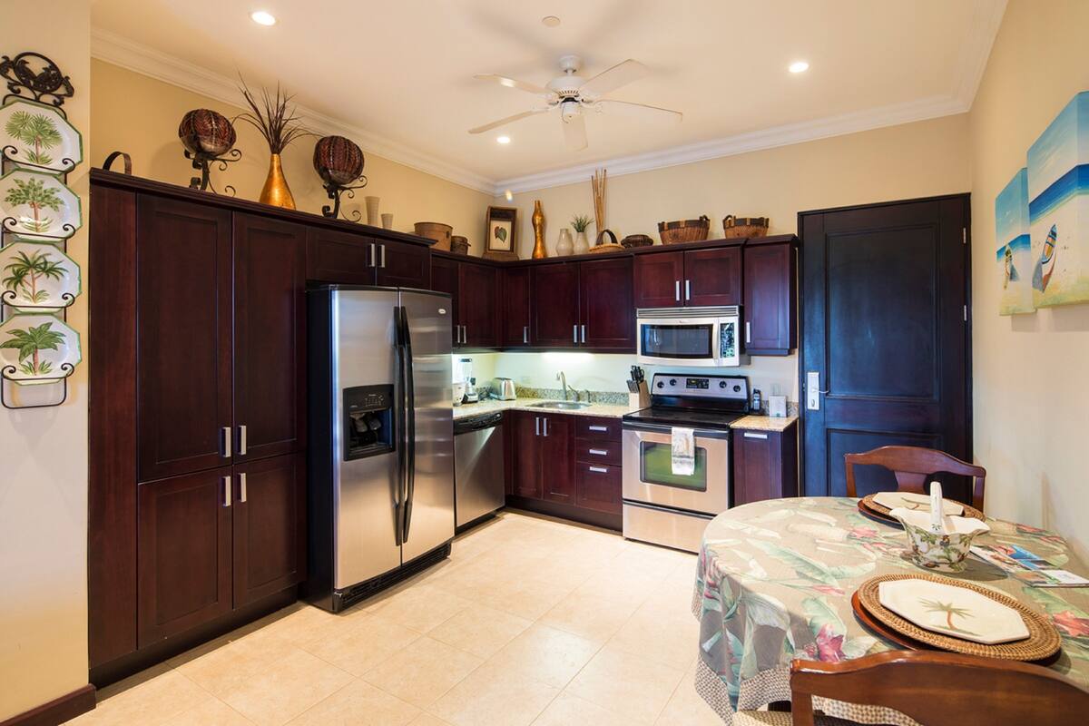 A kitchen with dark wood cabinets, stainless steel appliances, a microwave, and a dining area with a table set for two.