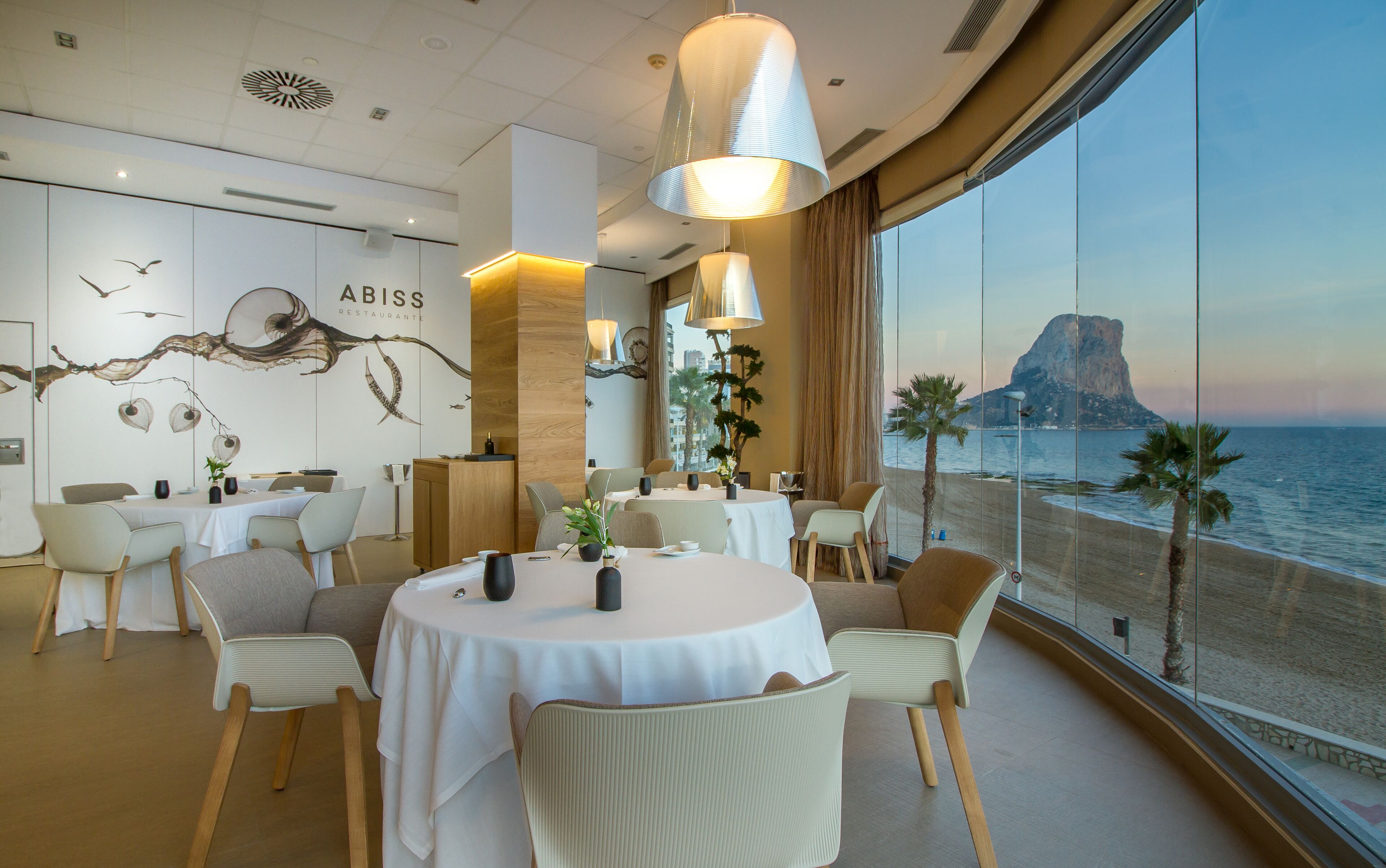 A modern dining area with round tables, chairs, and a view of the sea.