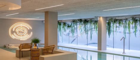 A modern indoor pool area with a seating area, a circular light installation, and hanging plants.