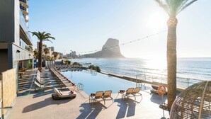 Un área de piscina en la azotea con sillones, una palmera y vista al océano.