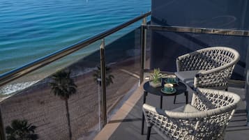 Uma varanda com cadeiras de vime, uma pequena mesa e vista para a praia e o oceano.