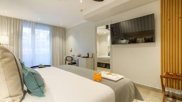 A modern hotel room with a large bed, a desk, a TV, and a wardrobe.
