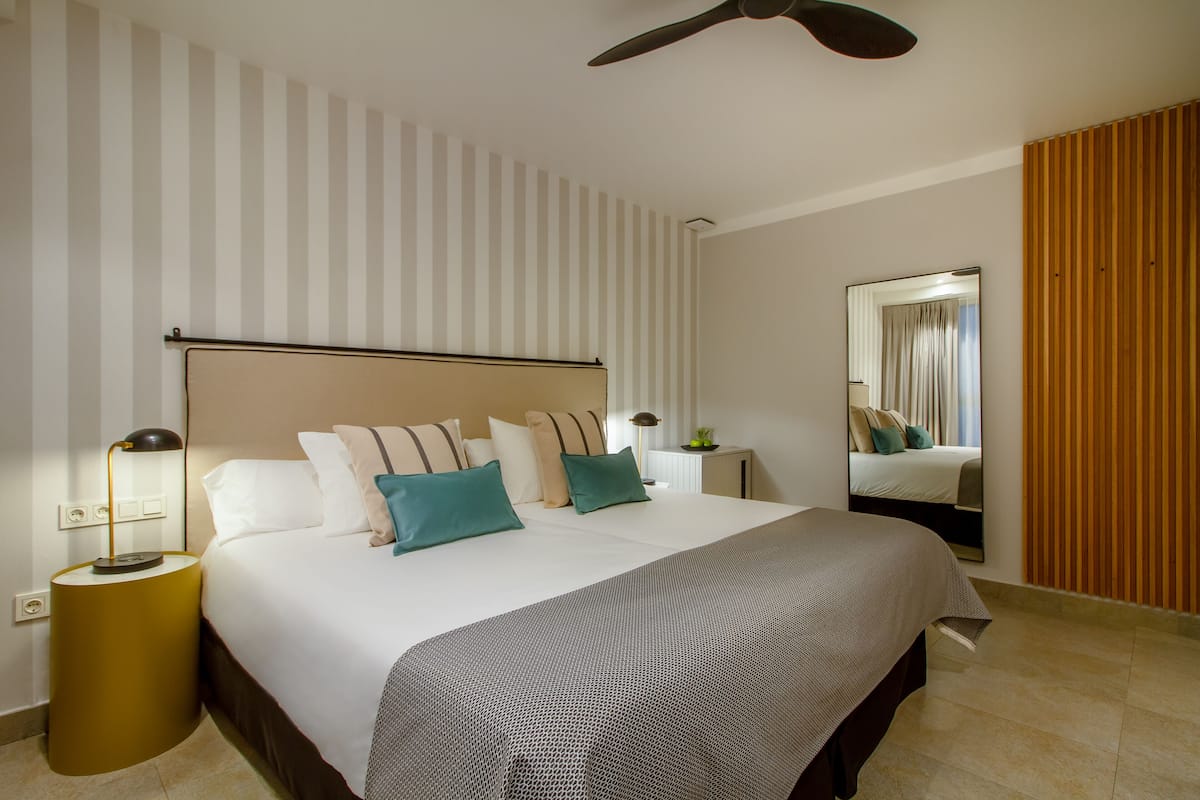 A hotel room with a large bed, a bedside table with a lamp, a ceiling fan, and a mirror on the wall.