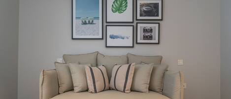 A living room with a beige sofa, a coffee table with two green apples, and four framed pictures on the wall.