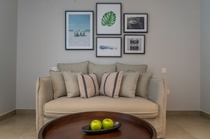 Una sala de estar con un sofá color beige, una mesa de centro con dos manzanas verdes y cuatro cuadros en la pared.