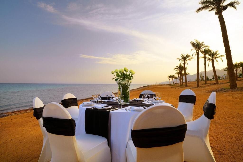 Une table dressée pour un repas sur une plage, avec des palmiers en arrière-plan.
