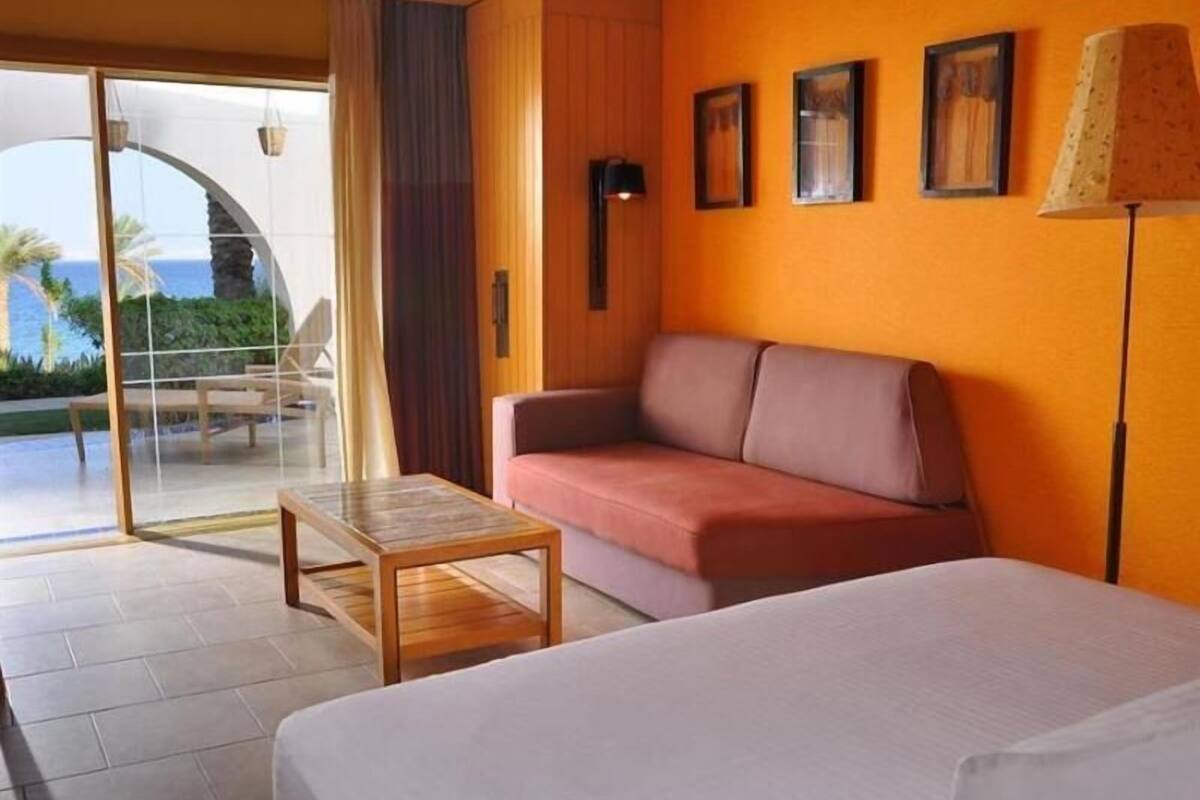 Ein Hotelzimmer mit Bett, Sofa, kleinem Tisch und Meerblick durch eine Glastür.