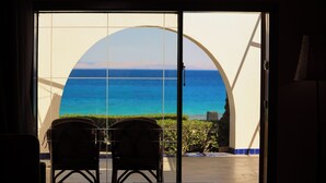 Habitación con vista al océano a través de un gran ventanal, dos sillas y una mesita.