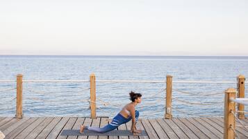 A person performing a yoga pose on a wooden deck with a view of the sea.