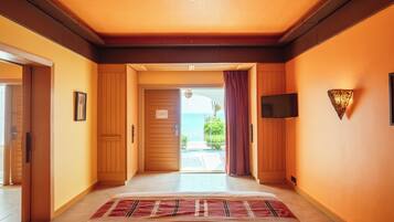 A hotel room with a bed, a television, a view of the sea, and a door leading to a balcony.
