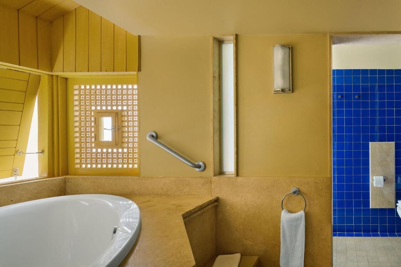 Un baño con bañera, barra de apoyo, argolla para toallas y pared con azulejos azules.