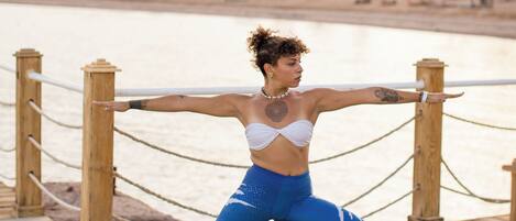 A person performing a yoga pose on a wooden deck with a river and mountains in the background.