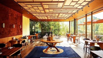 A modern restaurant with a wooden ceiling, large windows, and a central round table.