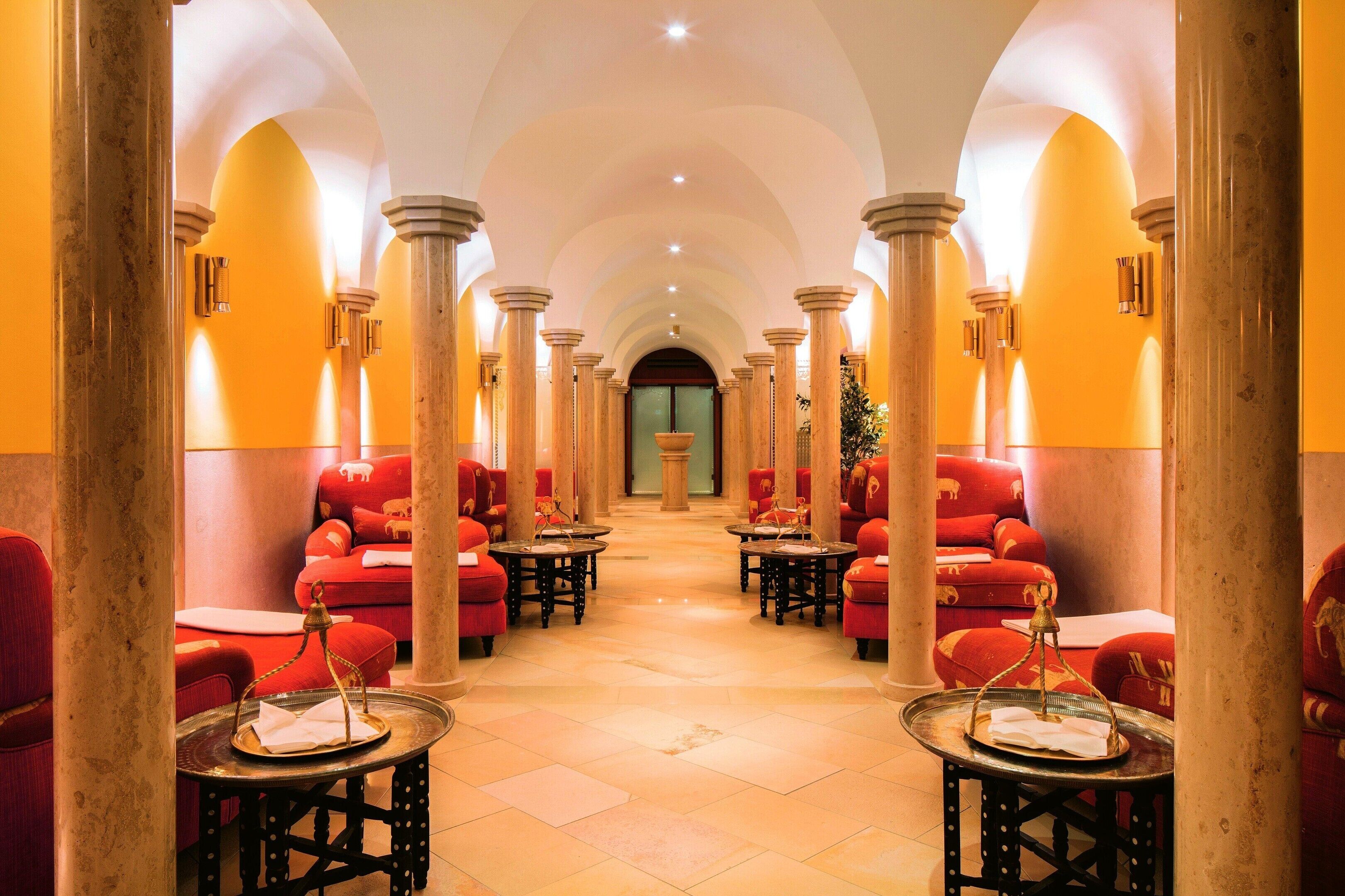 Ein Hotelkorridor mit roten Sofas, runden Tischen und Säulen.