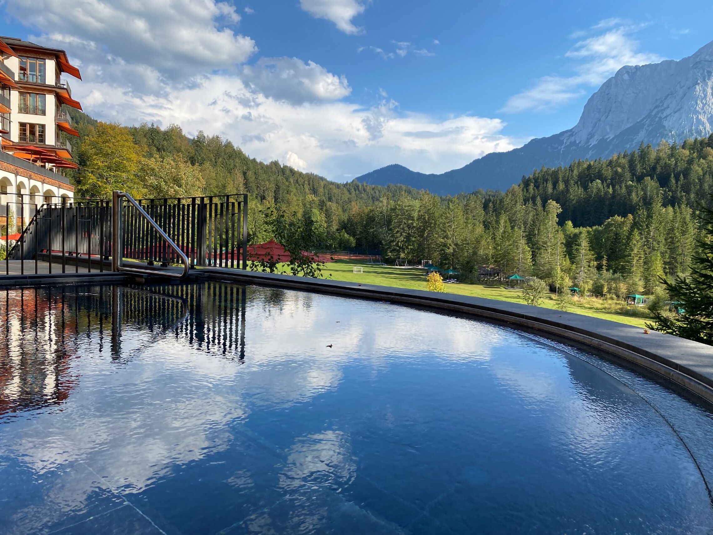 A swimming pool with a mountain view, a building with balconies, and a forested hillside.