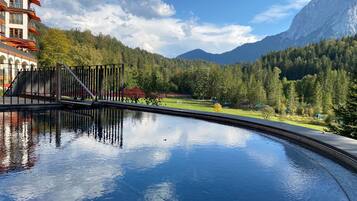 A swimming pool with a mountain view, a building with balconies, and a forested hillside.