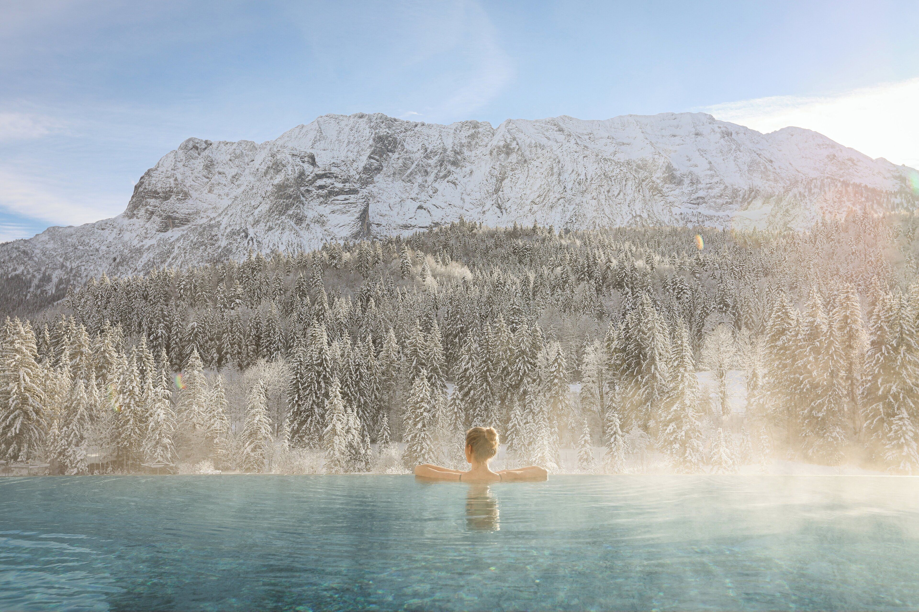 A person in a clear pool with a mountainous backdrop.