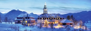 A large, multi-story building with a prominent tower, surrounded by snow-covered trees and mountains. - Schloss Elmau Luxury Spa Retreat & Cultural Hideaway (Kruen)