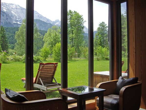 A room with large windows offering a view of a green landscape and mountains. There is a wooden chair and a small table with a glass top. - Schloss Elmau Luxury Spa Retreat & Cultural Hideaway (Kruen)