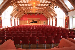 A large hall with rows of red chairs, a stage with a piano, and wooden beams on the ceiling. - Schloss Elmau Luxury Spa Retreat & Cultural Hideaway (Kruen)