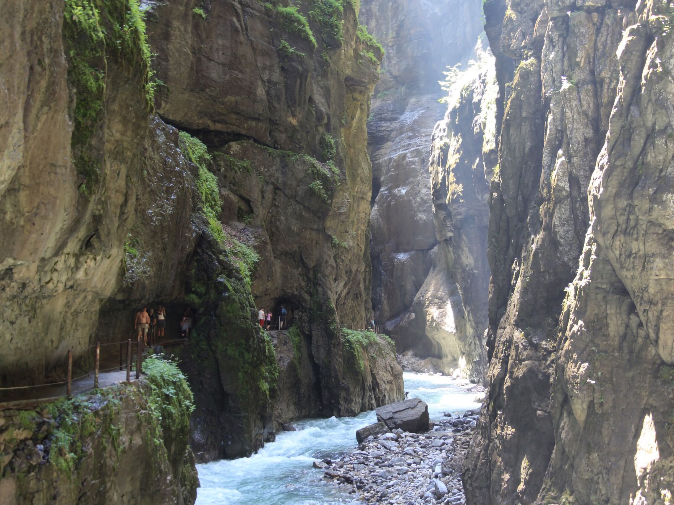 A narrow canyon with steep rock walls, a flowing river, and a viewing platform with people.
