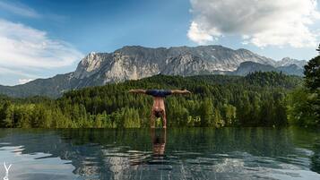 Una persona haciendo una postura de parada de manos en una piscina cristalina y reflectante, con un paisaje montañoso al fondo.