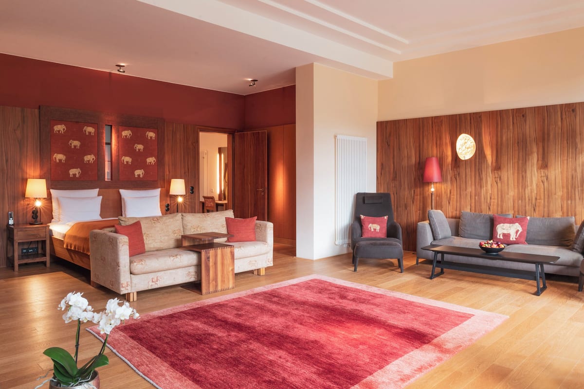 A spacious living room with a red rug, a sofa, a chair, and a coffee table. There is a fireplace with a red lamp and a wooden wall with animal prints.