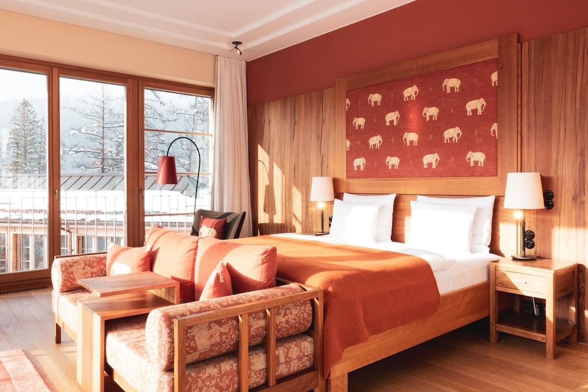 A hotel room with a large bed, a sofa, a small table, and a nightstand.