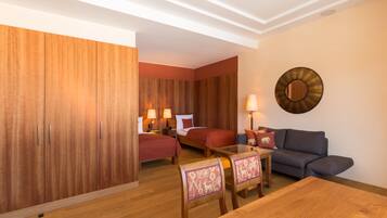 Habitación de hotel con suelo de madera, cama con ropa de cama roja, un sofá, una mesa y una lámpara de pared.