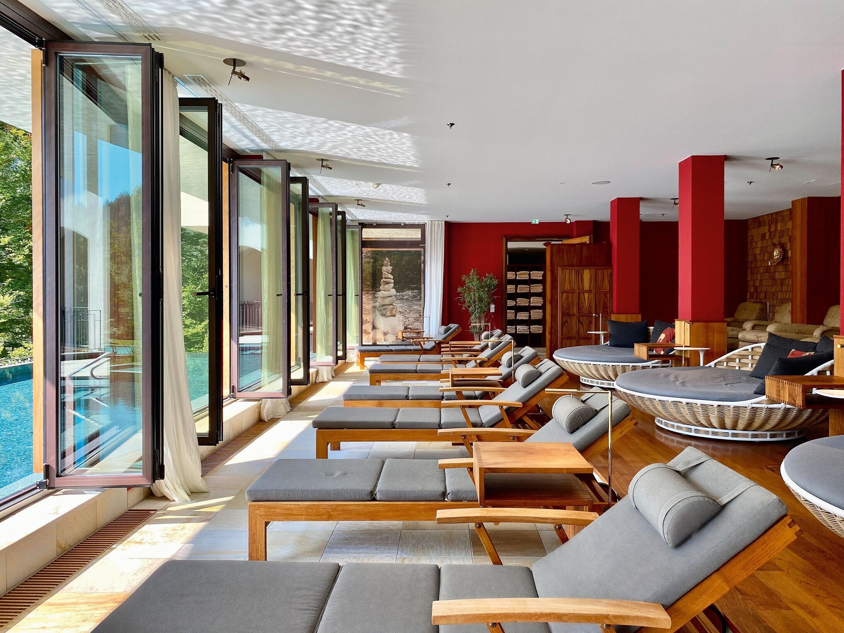 Ein sonnendurchflutetes Zimmer mit großen Fenstern, einem Pool und Liegestühlen.